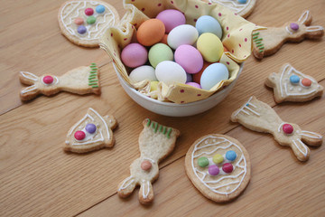 Decorated Easter cookies in shape of bunny with multi colored chocolate eggs on wooden table