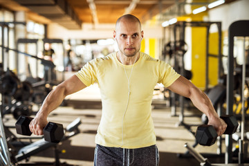 Fototapeta na wymiar Portrait of strong muscular active healthy young man raising dumbbells with open arms and listening music in the gym.