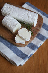 Fresh goat cheese with rosemary on a wooden cutting board on wooden table