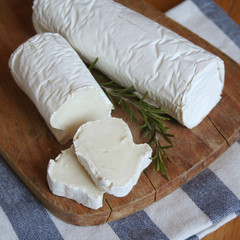 Fresh goat cheese with rosemary on a wooden cutting board on wooden table