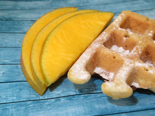 Belgian waffles and slices of fresh mango on a blue wooden table