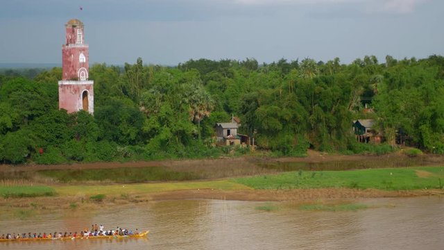 rowers training on river passing by an old lookout tower by the riverside