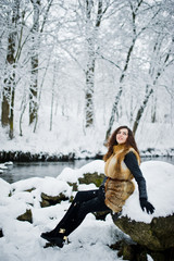 Fototapeta na wymiar Elegance curly girl in fur coat at snowy forest park at winter.