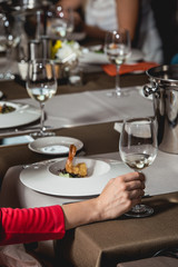 woman holds glass of white wine. people consider the color of the wine and try how it smells in different glasses