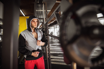 Fototapeta na wymiar Close up portrait of focused and motivated muscular hooded man standing with earphones in the modern gym.