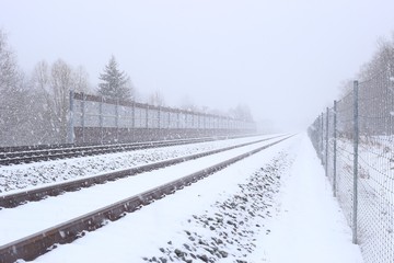 Snowy railway with noise damping wall in winter. Rail Baltica railroad protective fences.