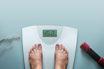 Exercising and Diet Concept, Woman Standing on Digital Weight Scales in House, Surrounded by Dumbbell and Measuring Tape. Modern Female's Lifestyle. Top View