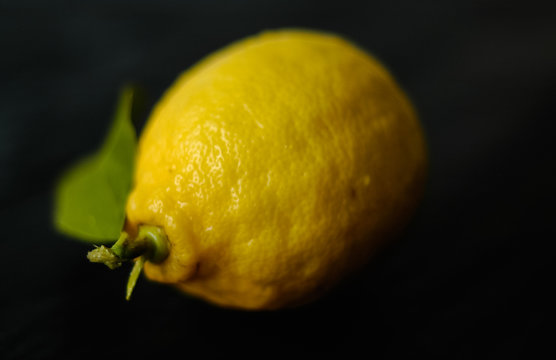 Close up macro shot of whole, ripe, organic lemon with green leaf and water drops on black background