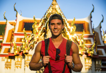 Young handsome man holding backpack standing in Grand Palace. In Bangkok, Thailand. Vertical...