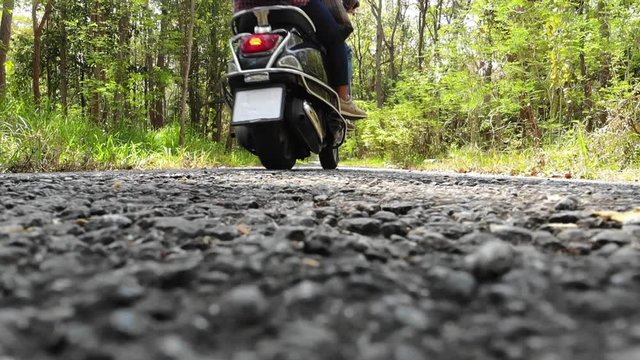 Slow motion Couple riding their scooter through forest.