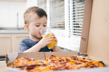 baby in the kitchen drinking orange juice and eating a large pizza