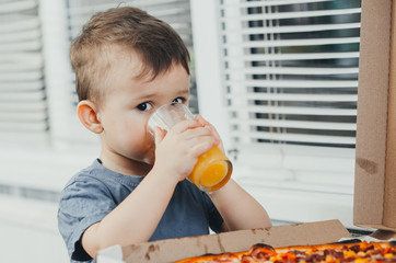 baby in the kitchen drinking orange juice and eating a large pizza