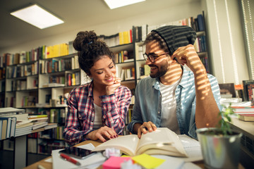 Close up of adorable cute stylish high school student couple flirting and talking in the library while learning together.