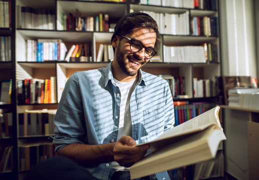 Handsome man hipster reading book at library smiling. Education at public.