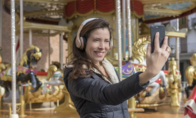 joy, woman next to a merry-go-round taking selfie with the cell phone on a spring afternoon. image of freshness and lifestyle in europe