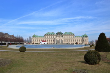 Piękny pałac w Wiedniu, stolicy Austrii, na pierwszym planie zadbany ogród z przystrzyżoną trawą i krzewami, kamienna sadzawka, błękitne niebo  - obrazy, fototapety, plakaty