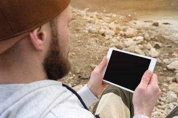 Close-up of a horde in a brown cap in the open air holds a white tablet pc in his hands. A bearded man looks at the tablet. OTS view from behind the shoulder