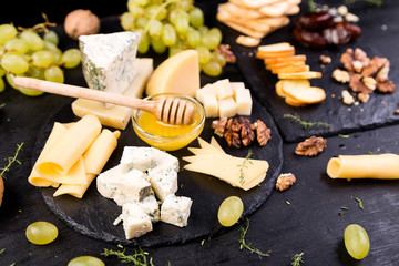 Cheese plate. Assortment of cheese with walnuts, bread an honey on stone slate plate.
