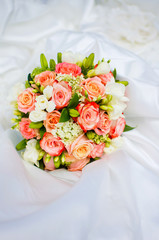 Closeup view of beautiful colorful bridal bouquet isolated on white fabric of dress of bride.. Vertical color image.