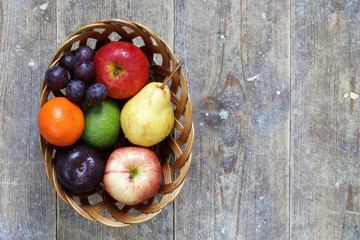 Mixed fruits of apples, lime, lemon, pears and plums in wicker bowl on wood table with copy space right