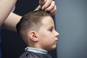 Barber making hairstyle to a Caucasian boy using hair gel.