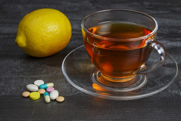 A pile of pills with a cup of tea and lemon