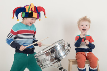 Two Happy Caucasian child drummer in a carnivalous fool's cap plays on a new drum set. Parents bought the boy a drum for training. Kids in bright clothes with new sticks in his hands be happy at home