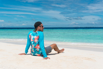 Man sit on sandy beach with transparent water of ocean in Maldives island
