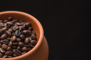 Clay pot filled with coffee beans on black background. Place for text