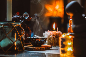 hot tea into little tea bowl, steam, burning candle, on wooden coaster among decoration, warm cozy atmosphere