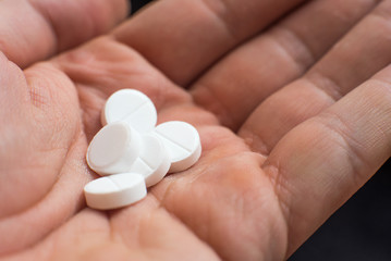 White pills in hand on black background closeup