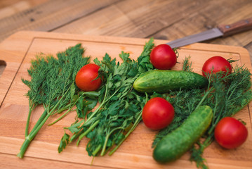 Cherry tomatoes, cucumbers, dill and parsley on wooden board on table with knife closeup. Healthy food concept.