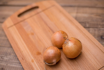 Three onions on cutting board on wooden table. Place for text or design