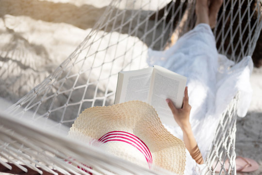 Young lady reading a book in hammock on tropical sandy beach.