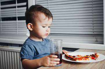 at night, the child himself in the kitchen drinking juice and eating pizza