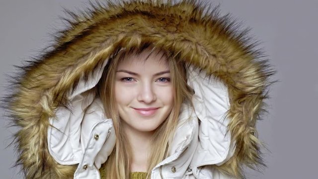 Closeup of blond woman wearing warm winter coat with fur hood on smiling at camera and winking