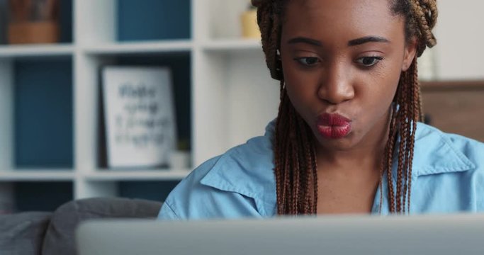 Attractive young African American woman with trendy dreadlocks cheerfully uses the laptop. Internet surfing, social network. Close up view, camera stabilizer shot