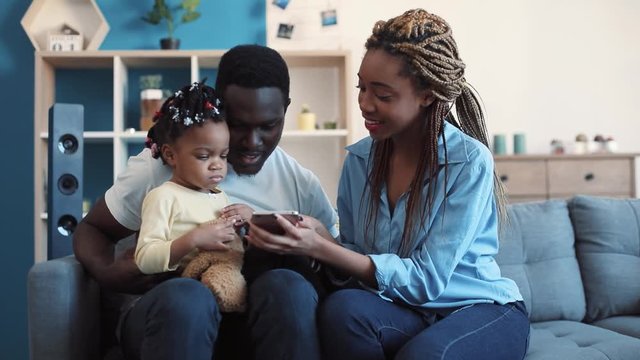 Lovely African American parents show cartoons on the portable device to their cute toddler. Happy moments, childhood memories. Close up view, camera stabilizer shot