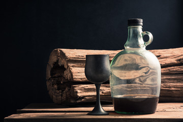 aged metal wine glass and wine bottle with tree stump at back with space of dark background