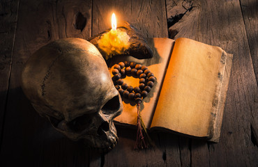 still life photography : human skull with wood beads rosary on the blank old book in mood of burning candle light
