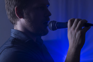 Photo of man singing to the microphone with blue lights in the background