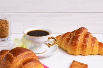 Stilllife of coffee cup with espresso, croissants, biscuits, tender flower, brown sugar on a wooden background