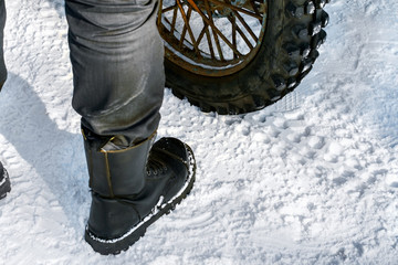 Motorcycle racing in the snow.A man is standing in the snow by his motorcycle. Fragment-foot in a sporty leather boot near the motorcycle wheel.