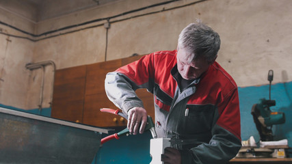 Worker assembling the metal part by hand with pliers, tools for grinding metal and metal details in the foreground