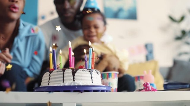 Close up view of birthday cake with multicolored burning candles, falling golden confetti, happy cute family blows out candles, laugh and cheerfully clap their hands. Party hard. Slow motion