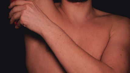 The body of a man, a man holds in his hand a red deodorant for the armpits, a black background.