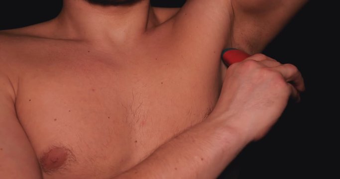The body of a man, a man holds in his hand a red deodorant for the armpits, a black background.