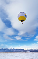 Hot air balloon with tourists in a basket against a blue sky with clouds. The shell of the ball depicts the official coat of arms of the Republic of Buryatia (not an object of copyright)