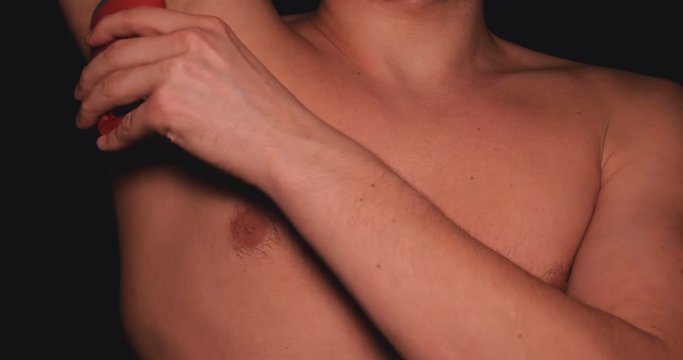 The body of a man, a man holds in his hand a red deodorant for the armpits, a black background.