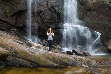 Young woman in namaste pose with waterfall behind